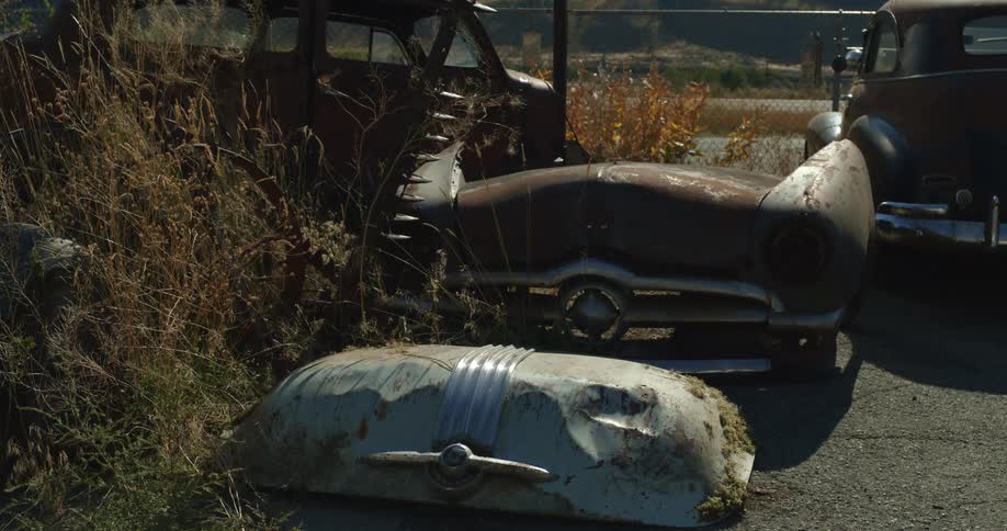 Old and rusty parts of classic cars in the back of a fenced lot in the daytime