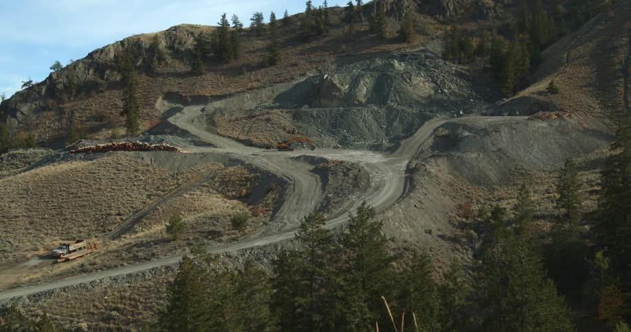 Excavators and trucks on a quarry on the side of a mountain at daytime
