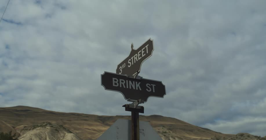 Street signs sit atop a stop sign at an intersection near a canyon