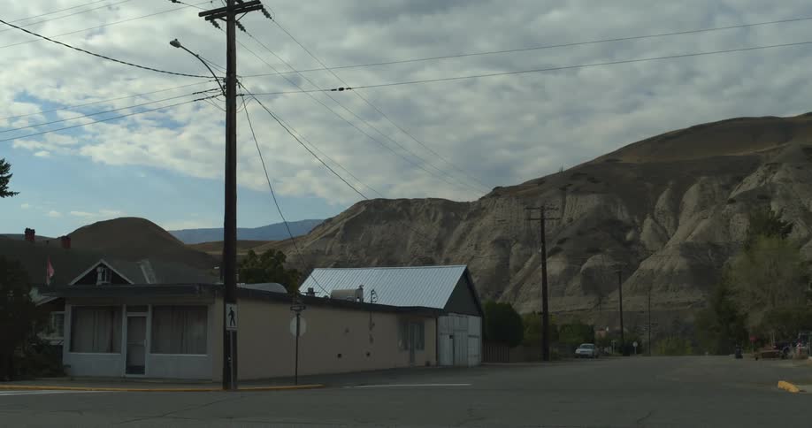 Dark blue hatchback car passes by buildings and utility pole standing against distant mountains