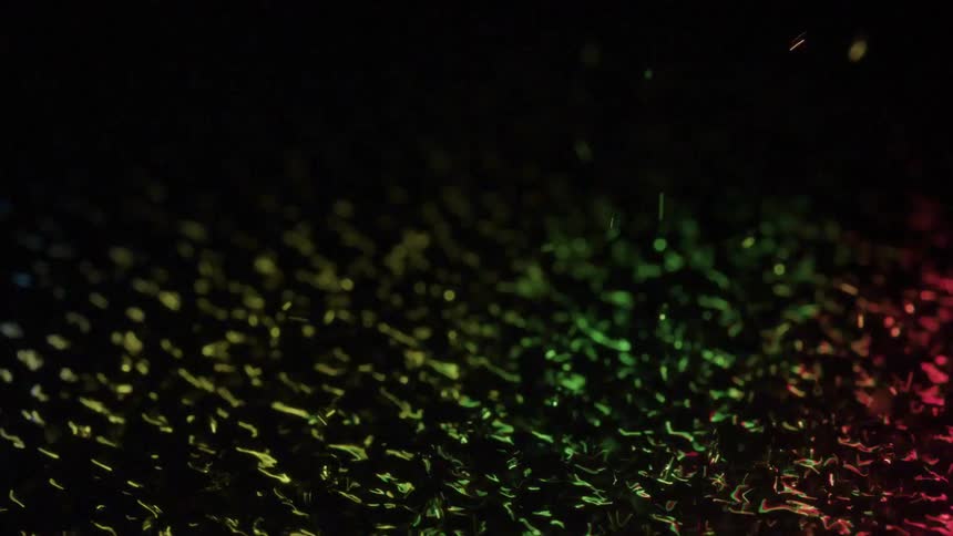 Colored light shines on water as it ripples and many spheres bounce from the water as colors vibrate in the ripples