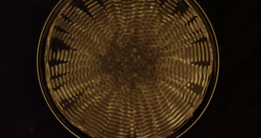 An up close of a glass of liquid that is being vibrated creating ripples on the surface of the liquid