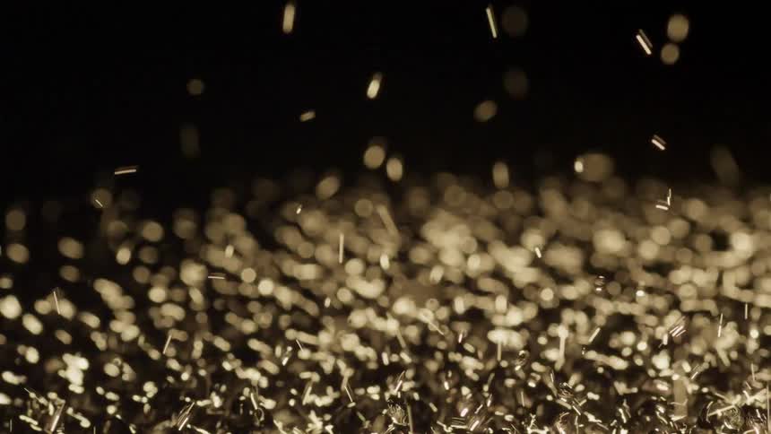 Light shines on golden particles as they bounce and vibrate in the darkness