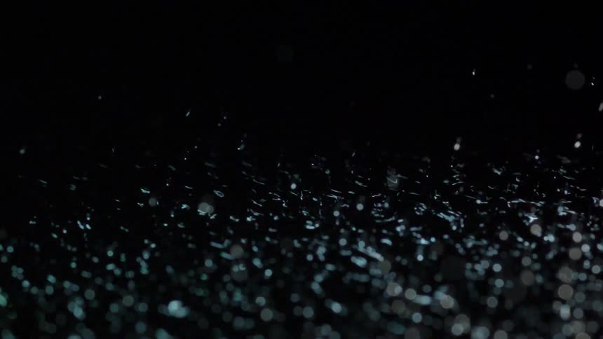 Water droplets are dancing above a vibrating pool of water in a dark studio environment with changing light colors