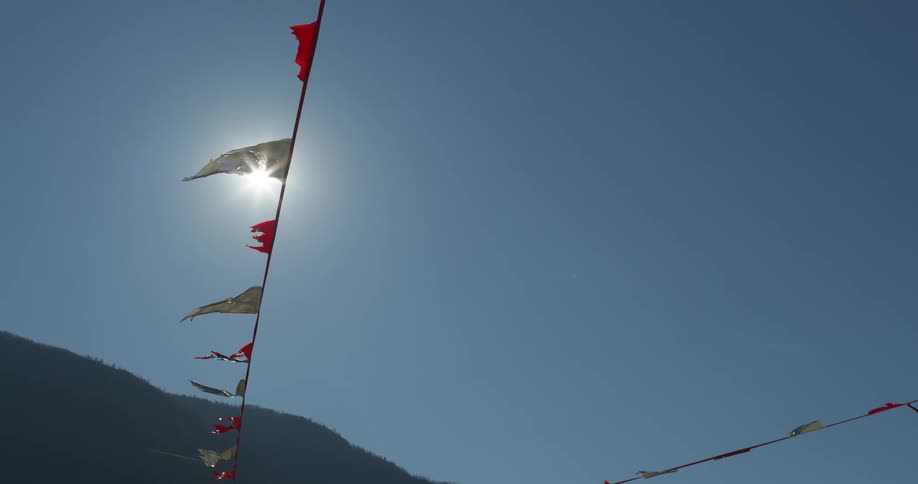 Tattered flags on a string with the sunlight beating down behind them