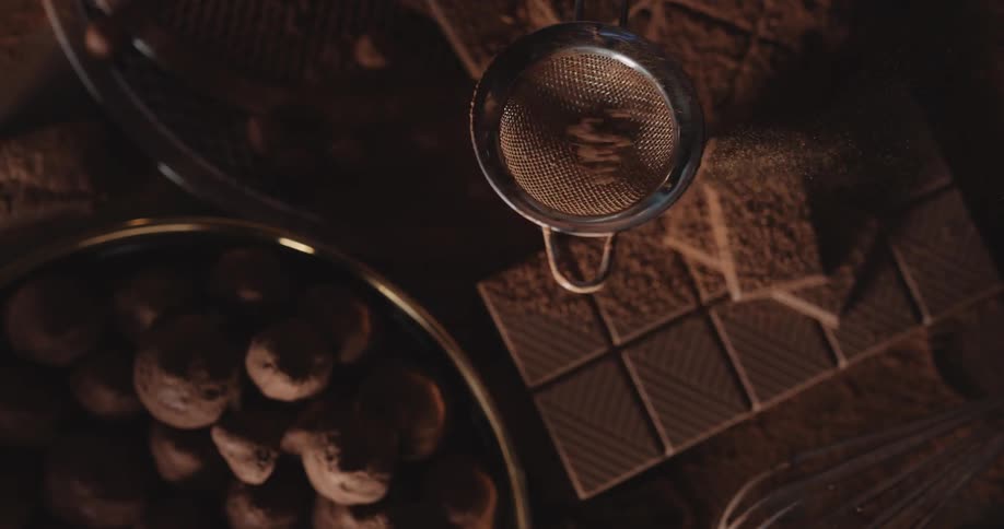 Someone is shaking a spice ball as powder falls onto cookies on a table