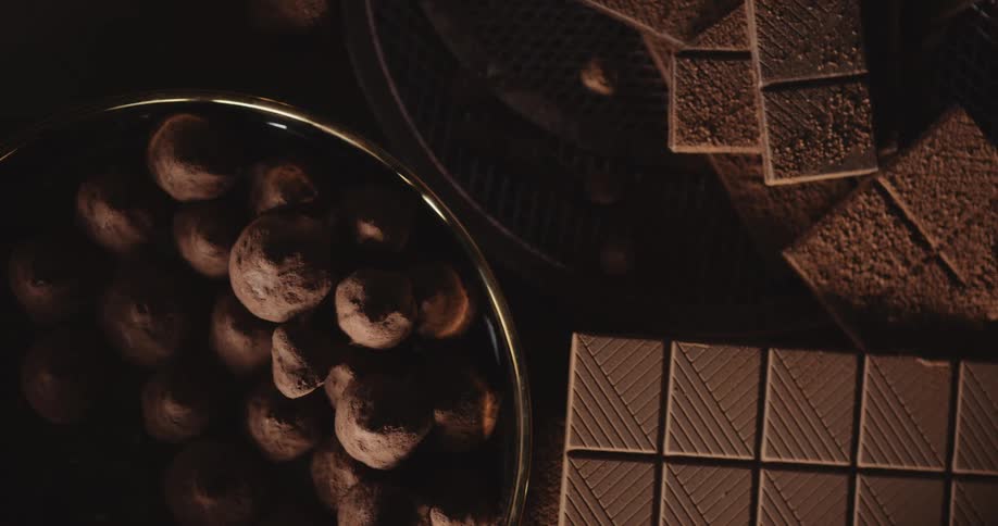 Chocolate candy is in a bowl on a table next to square chocolate cookies