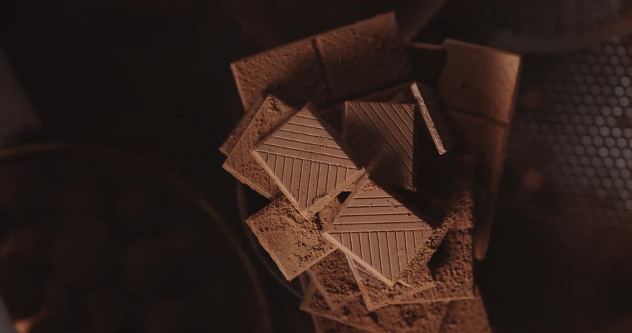Chocolate tablets broken in squares piled up surrounded by chocolate dust