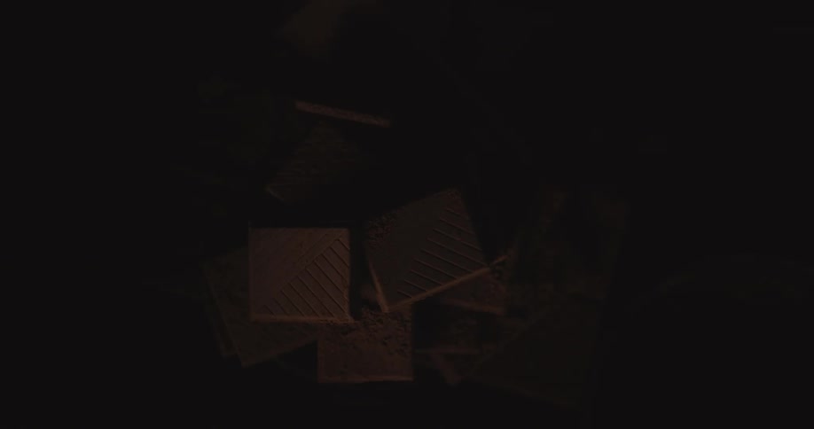 Light shines on square cookies that are stacked in a pile on a table in a dark room