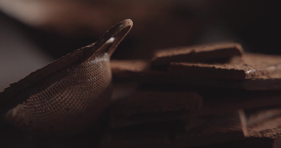 Person uses small mesh sieve to dust cocoa powder onto flat chocolate bars