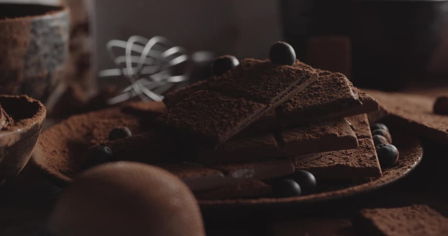 Light powder falls on to a plate of cookies and chocolate on a table with a wire whisk and bowls