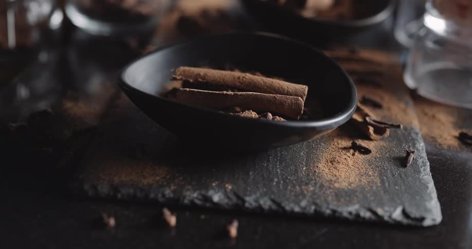 Two cinnamon sticks in black bowl on wooden table