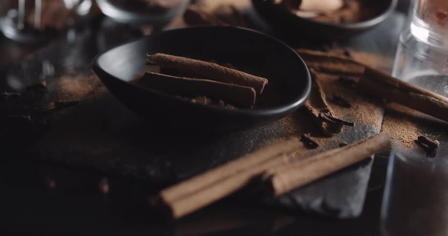 Two cinnamon sticks in black bowl and cinnamon powder on wooden table