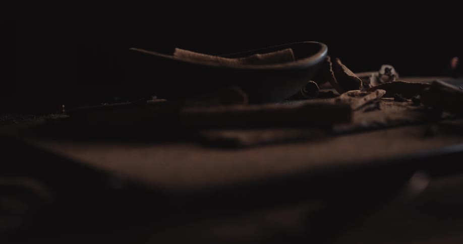 Light shines in a dark room revealing cinnamon sticks in a bowl and on a table