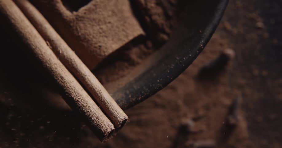 Ground cinnamon dust floats through air over bowl holding cinnamon stick and ground powder