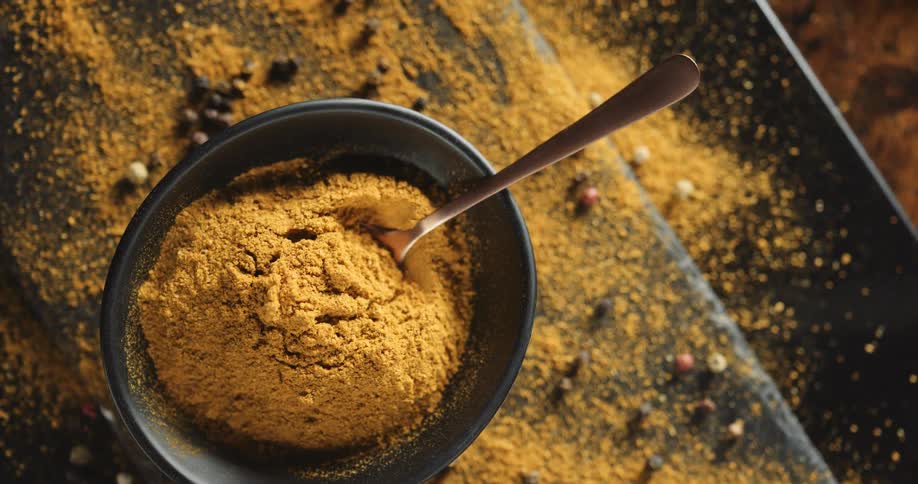 Bowls with cinnamon are on a table with a scoop and a spoon and cinnamon and chocolate are scattered on the table