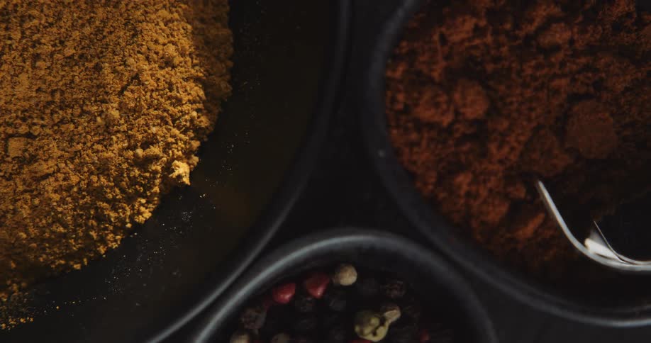 Shadows play over spices in bowls on dark surface