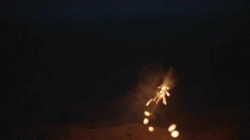 A person lights a bottle rocket on the beach at night