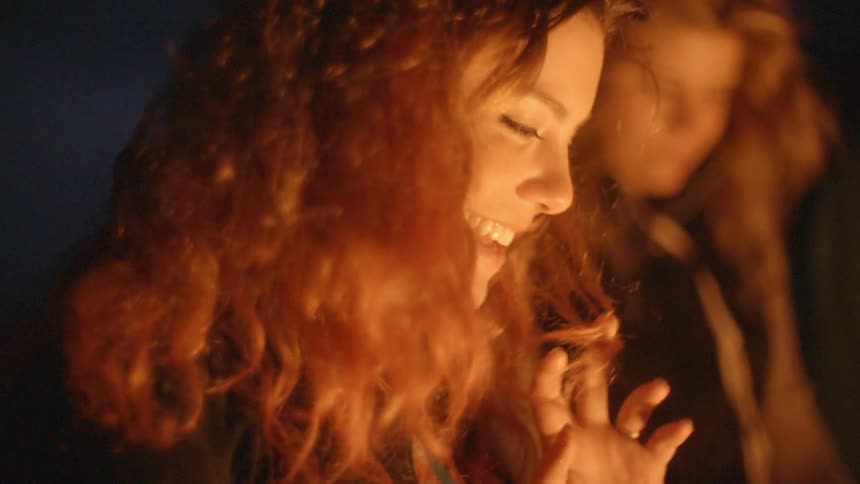 A woman smiling and looking down at a campfire while with her friends at night