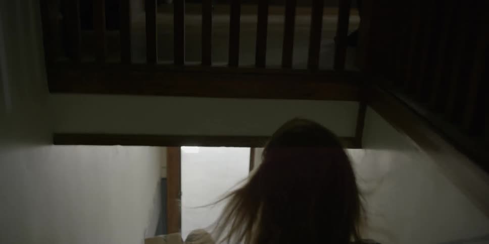 A woman quickly makes her way down stairs passing a man carrying up some boxes