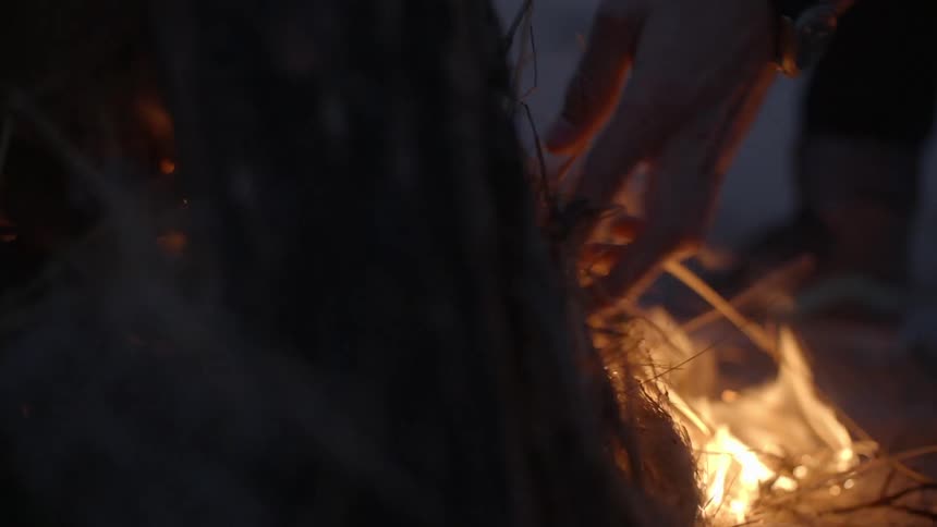 Hay is being added to a beach campfire at night