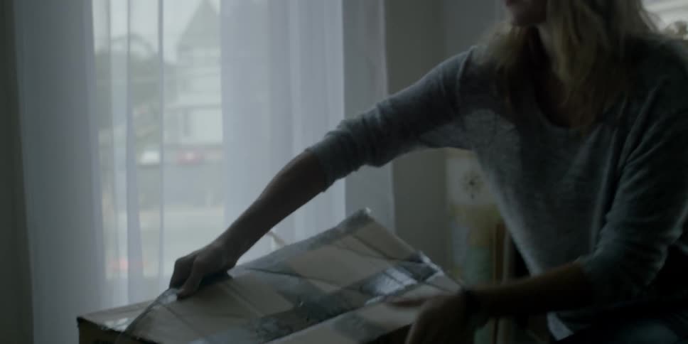 A woman opens a box near a window during the day