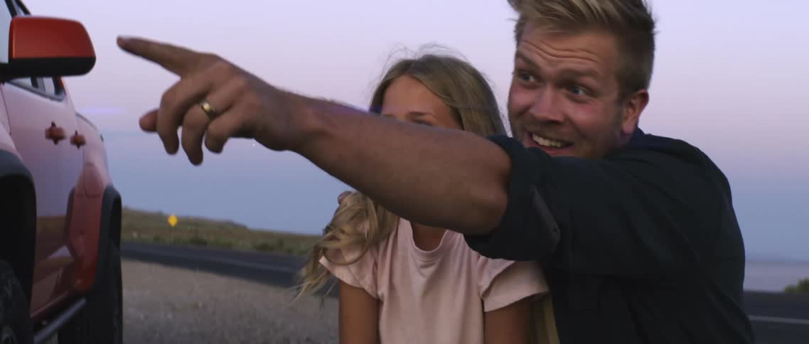 A smiling father and young daughter pointing and looking at something in the distance