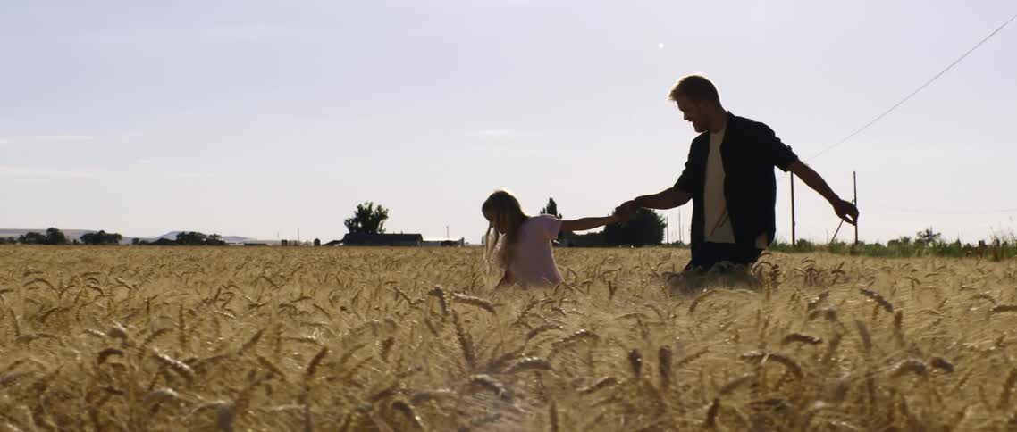 A girl leads a man by the hand through a field of wheat during the day