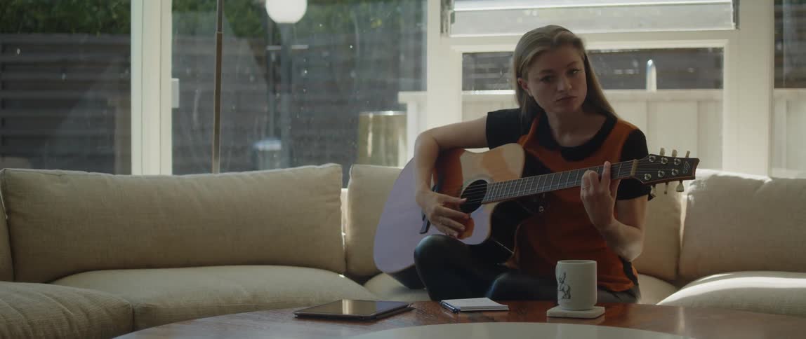Close up of a young woman playing acoustic guitar while writing a song at home