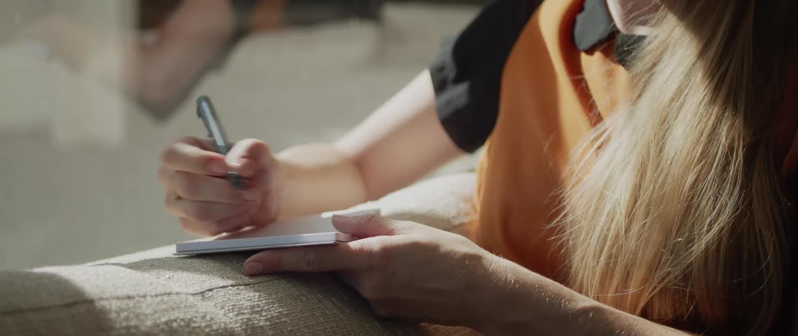 A woman is sitting on a couch and writing on paper