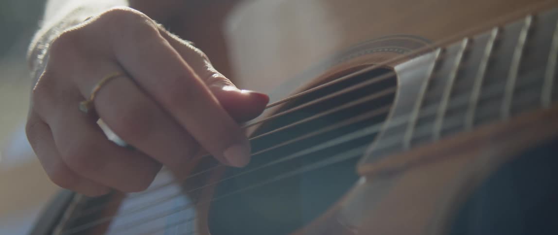 A woman strumming the strings of an acoustic guitar