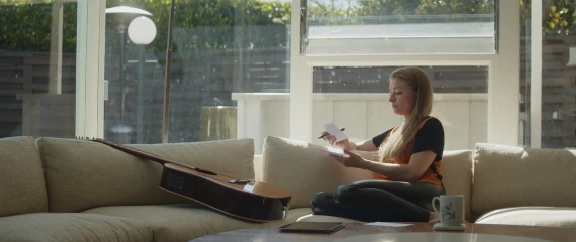 A woman is writing near her guitar