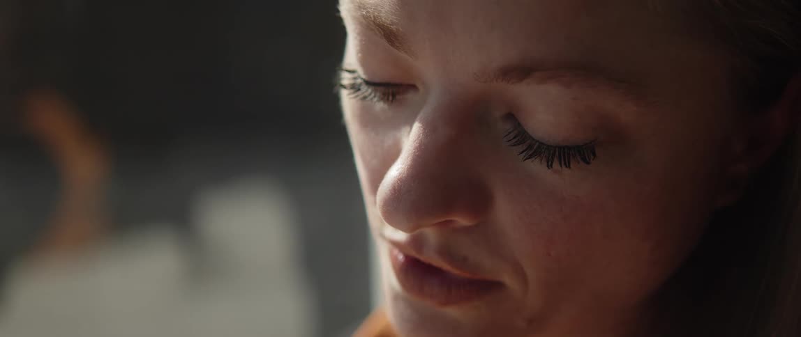 Light shines on a womans face as she is looking down at something and she looks up and then back down