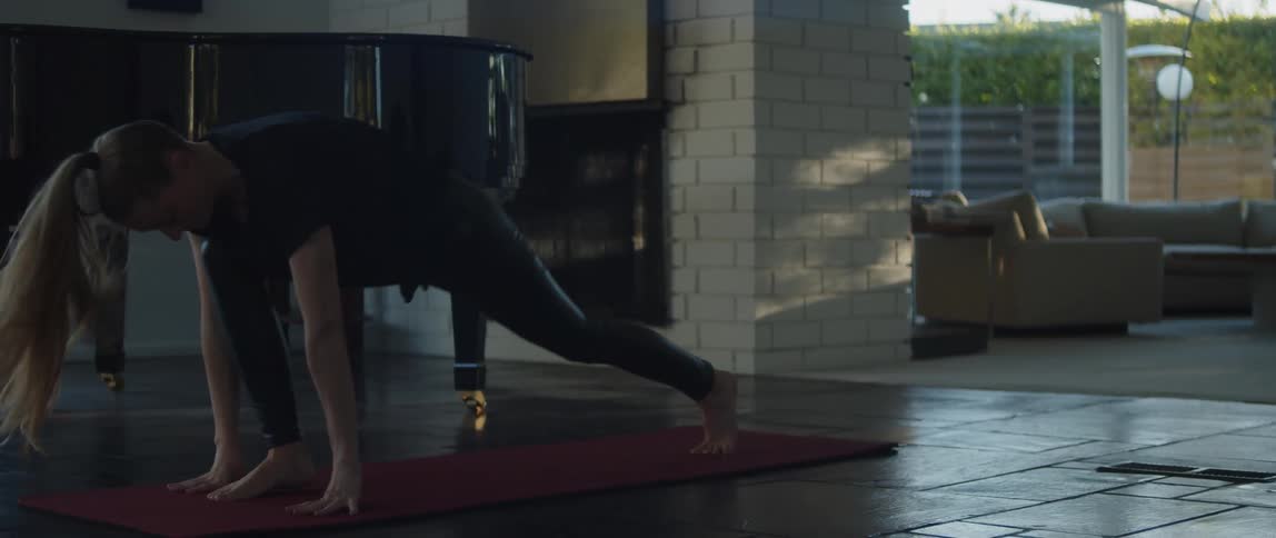 Blonde woman moves through yoga poses on yoga mat near piano in house