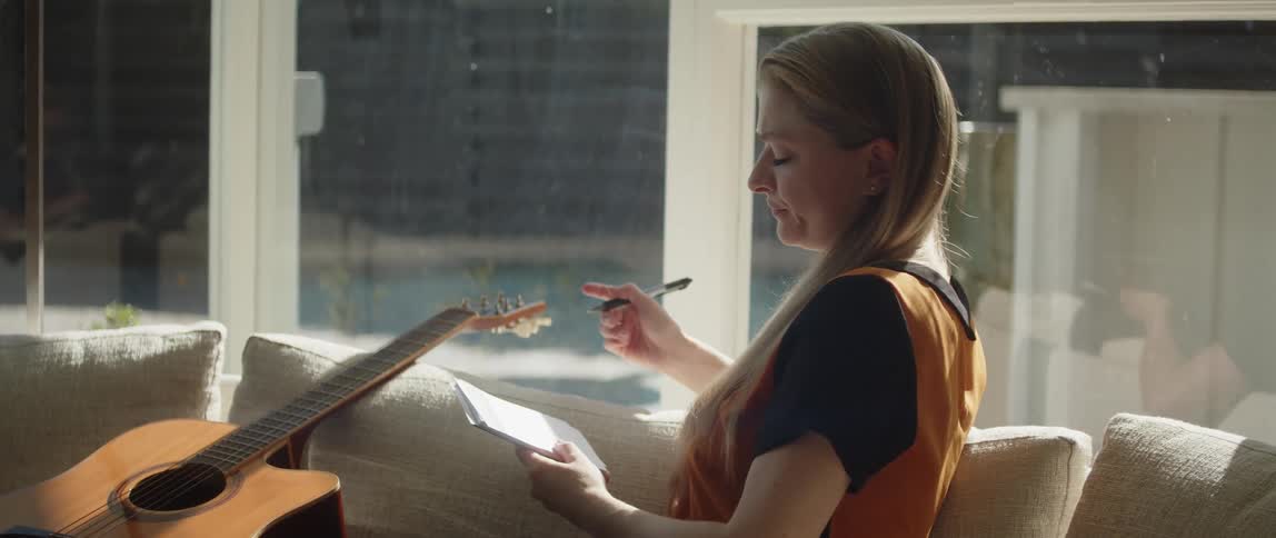 A woman is sitting on the couch with her guitar writing song lyrics