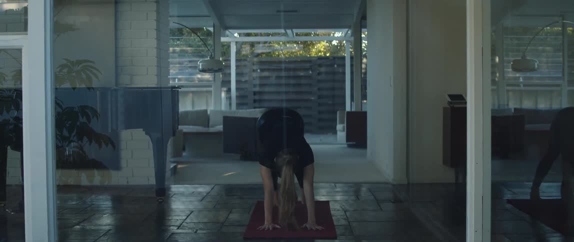 Blonde woman with ponytail black t shirt and yoga pants exercises on yoga mat in room