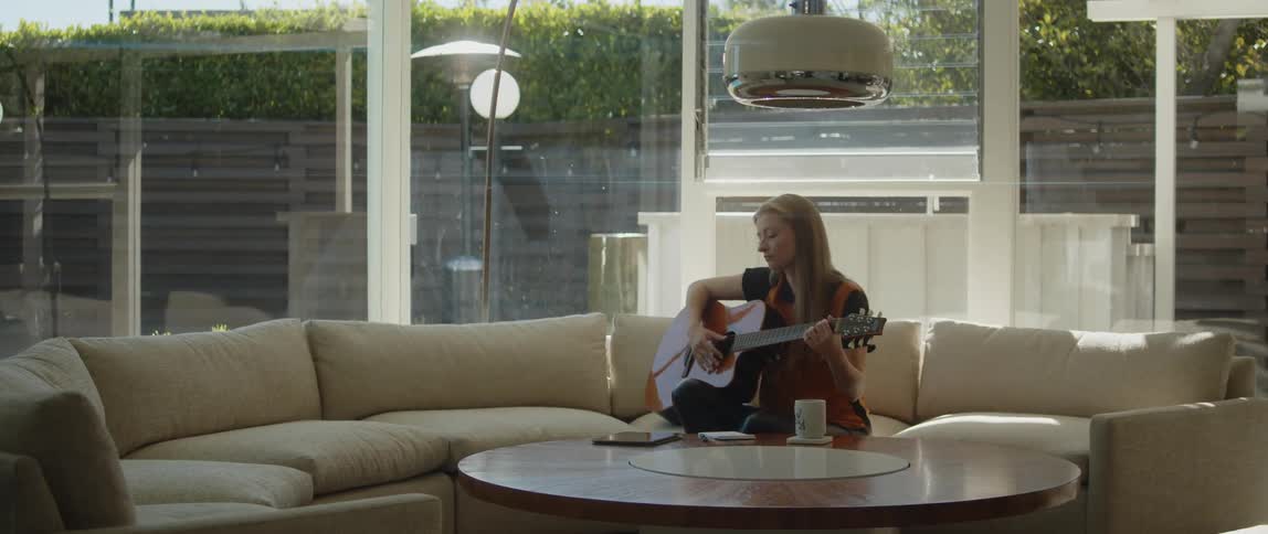 A woman is playing the guitar and sitting indoors