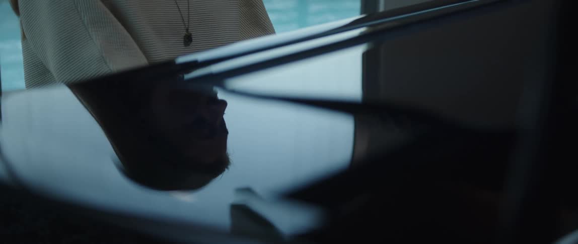The reflection of a womans face is seen on the piano as she plays