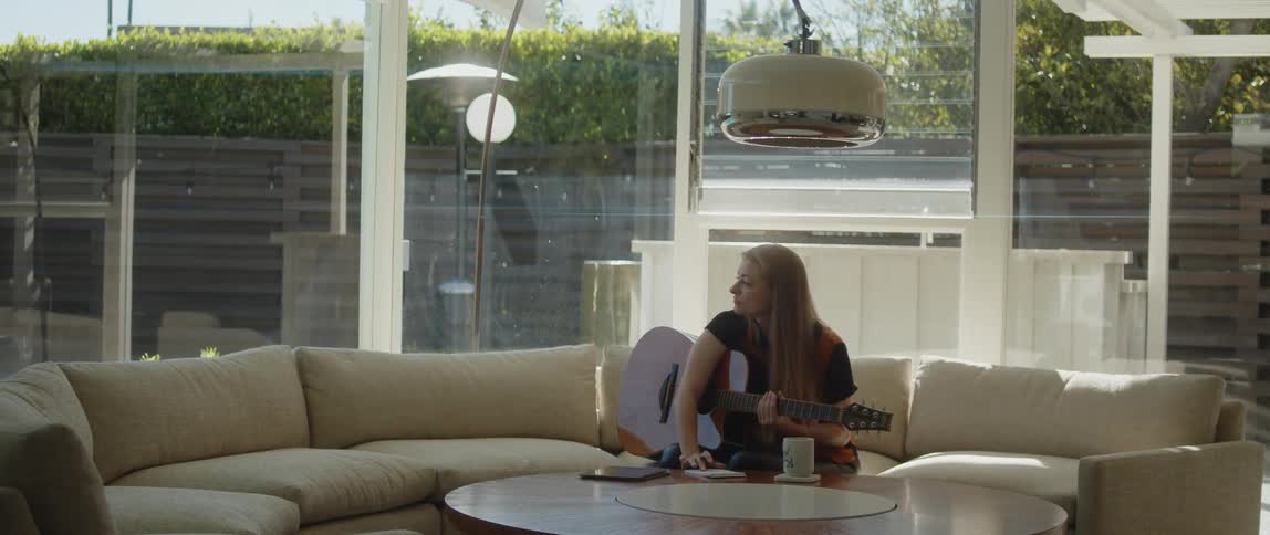 Female musician composes while sitting on couch with a guitar