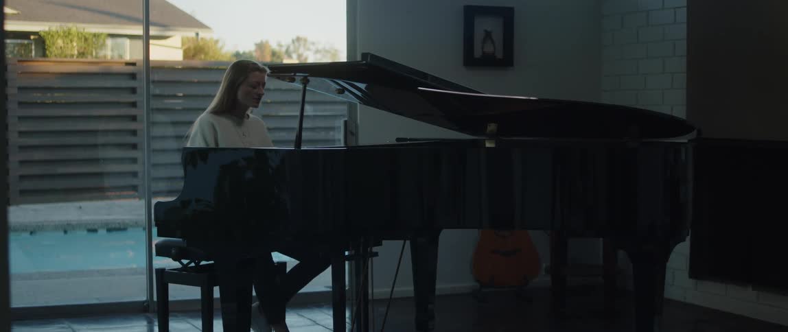 Blonde woman in white sweater plays grand piano and sing a song
