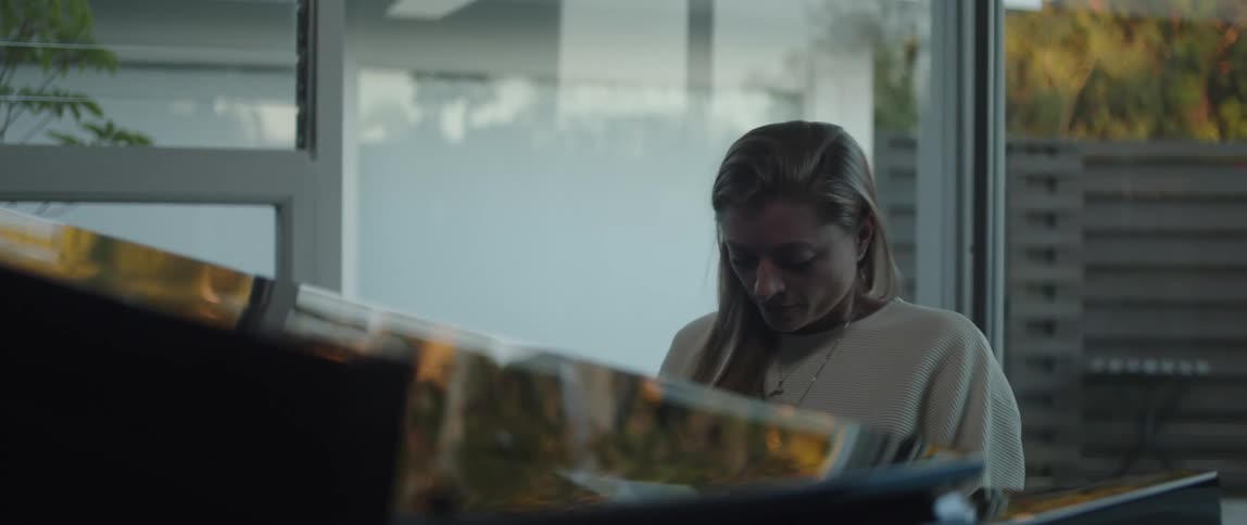 Woman with white sweater and necklace plays grand piano and gets up in living room at home