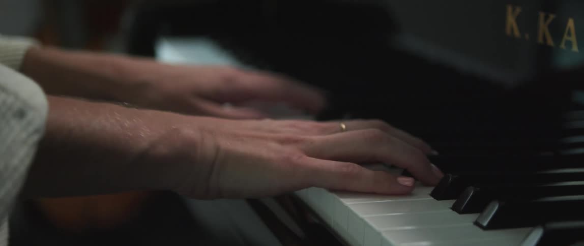 View of a womans hands as her fingers are pressing the keys of a piano as she plays
