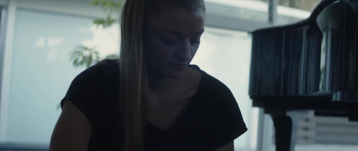 Blonde woman with ponytail black t shirt and yoga pants rolls yoga mat next to grand piano in room