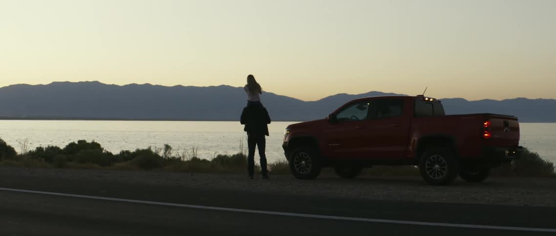 A father with his young daughter on his shoulders while parked next to a lake at sunset