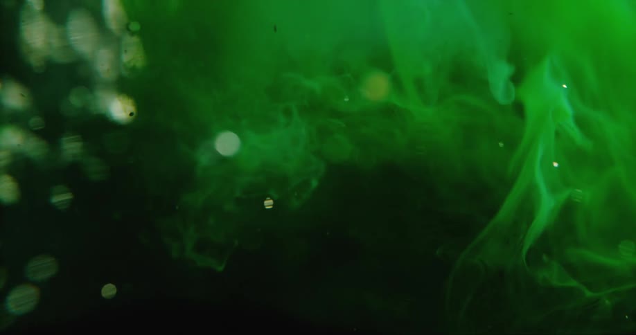 Green cloudy mass floats in clear liquid as spotsglare and glitter