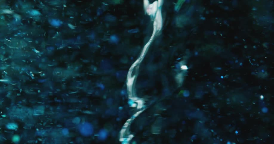 Blue tinted particles swirl around mass in liquid