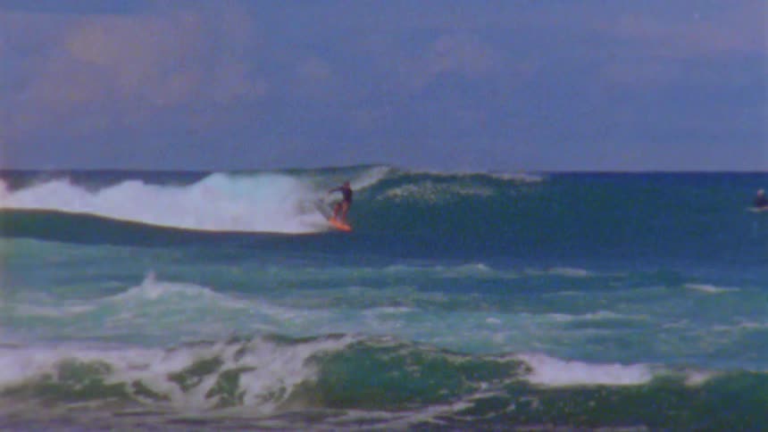 Far away surfer rides wave on surfboard seen from coast
