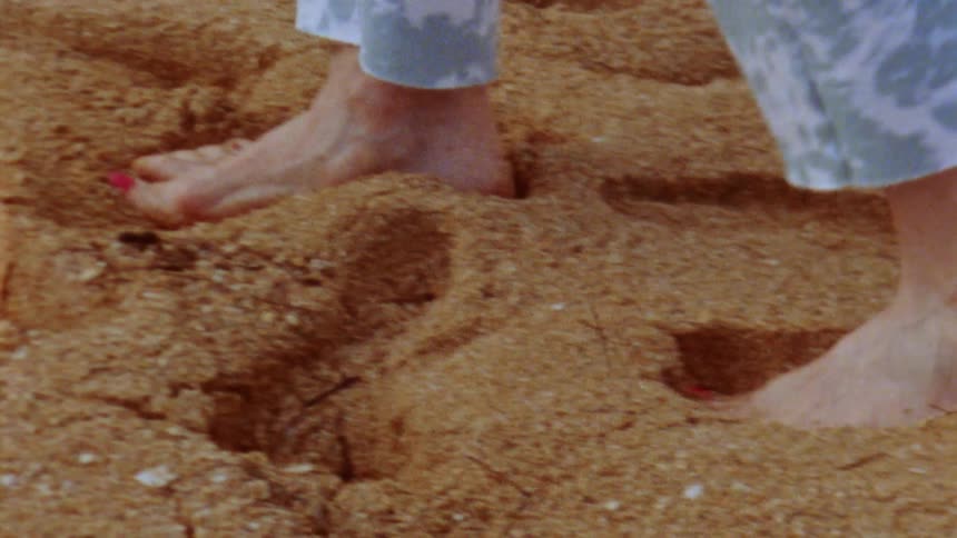 A person walks barefoot through a brown sand
