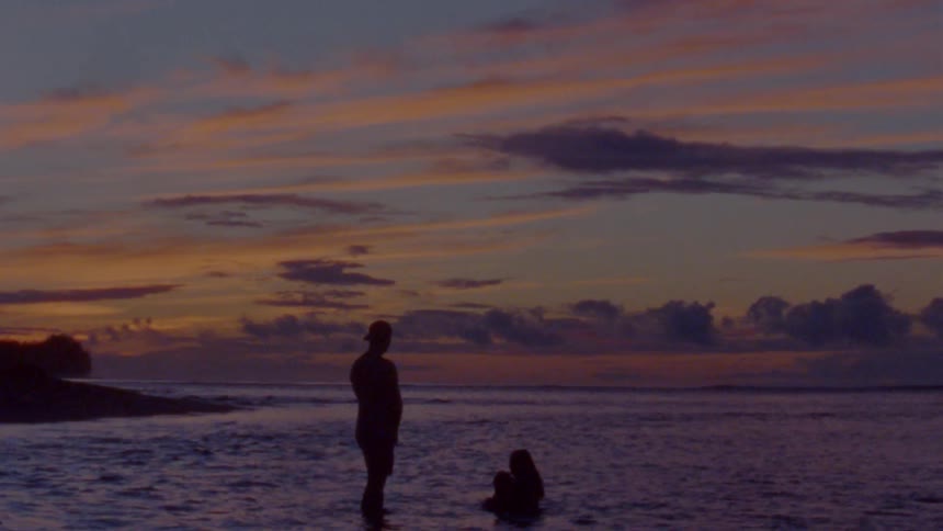 A mom and dad with their infant child on a beach at sunset