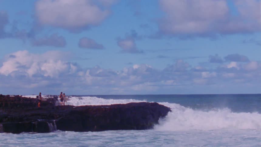 A group of surfers stands on cliff while ocean waves crash against the cliffside